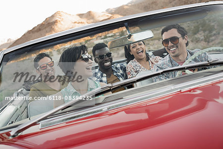 A group of friends in a red open top convertable classic car on a road trip.