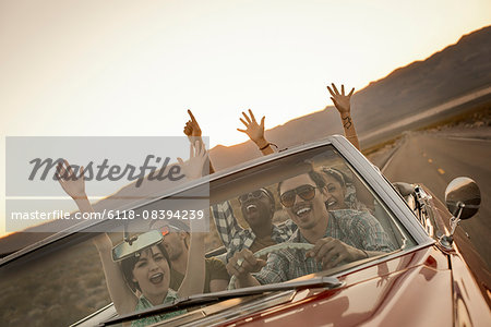 A group of friends in a red open top convertable classic car on a road trip.