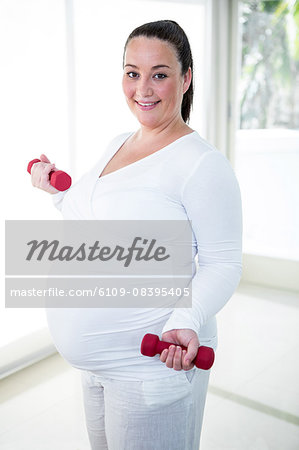 Pregnant smiling woman lifting dumbbell