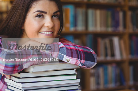 Happy female student leaning on book stack