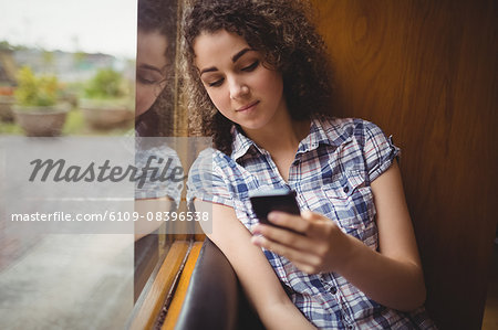 Pretty student sitting by the window using phone