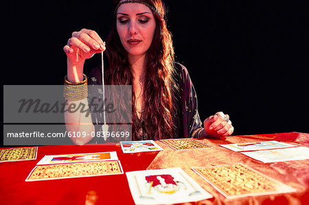 Female fortune teller using pendulum with eyes closed