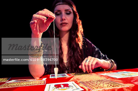 Female fortune teller holding pendulum with eyes closed