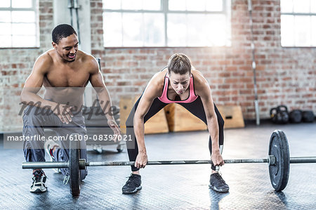 Trainer helping woman with lifting barbell