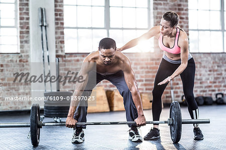 Female trainer helping fit man lifting barbell