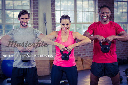 Three fit sporty people lifting kettlebell