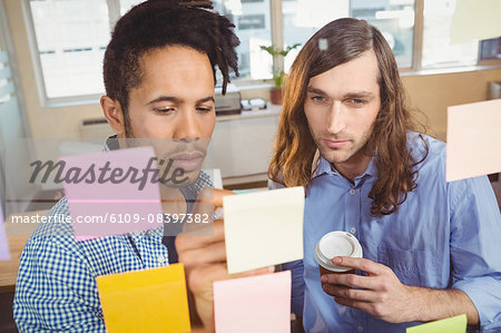 Businessman writing while colleague watching at adhesive notes