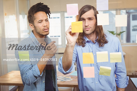 Businessman writing while colleague watching at sticky notes