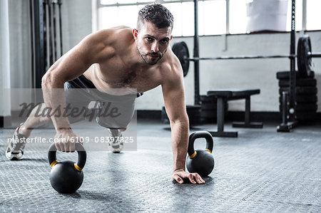 Fit shirtless man working out with kettlebells