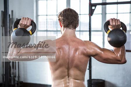 Fit shirtless man lifting kettlebells
