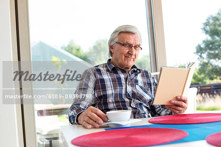 Old man having coffee while reading