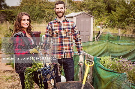 Couple with basket of vegetables and wheelbarrow