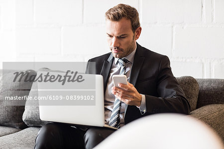 Focused businessman using laptop and smartphone