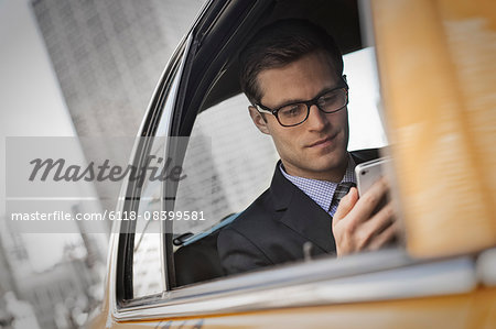 A working day. Businessman in a work suit sitting in a cab checking his phone.