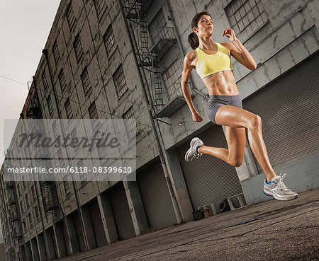 A woman running along an urban road, legs high and arms pumping.