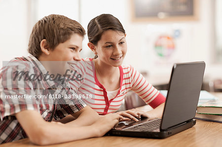 Two children, a boy and girl sitting at a desk, using a laptop computer.