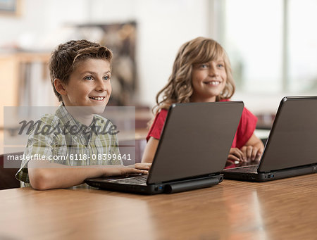 Two children seated at desks in class using laptop computers.