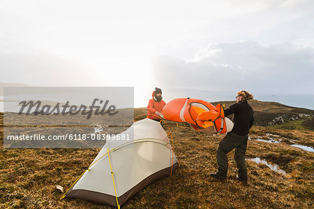 Two men holding and putting up a small tent in open space. Wild camping.