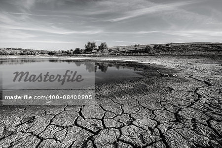 Drought. Chapped ground is in foreground. This is a coast of ephemeral impounded body. Black-and-white image.
