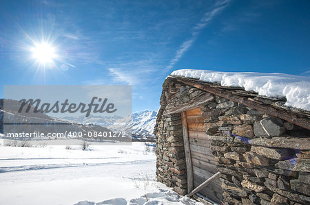 Remote alpine mountain hut on a slope in the sunlight covered with snow