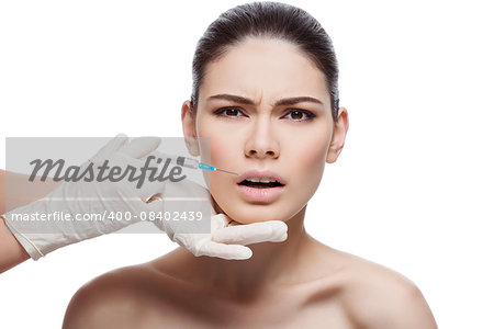 Beautiful young woman with expression of pain on face gets injection in lips from sergeant. Isolated over white background.