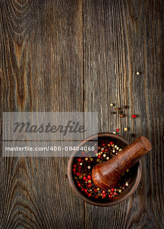 Colorful peppercorns in mortar on wooden background.