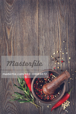 Fresh rosemary with chili  and peppercorns in mortar on wooden background.