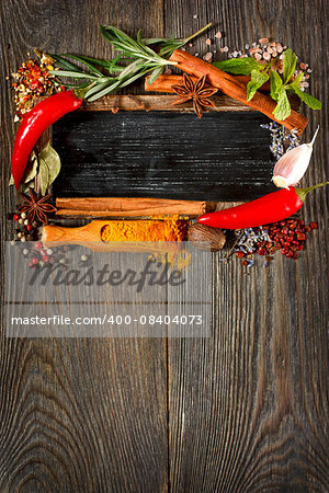 Colorful spices and herbs frame around chalk blackboard on a wooden background.