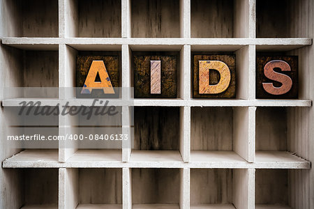 The word "AIDS" written in vintage ink stained wooden letterpress type in a partitioned printer's drawer.