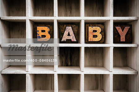 The word "BABY" written in vintage ink stained wooden letterpress type in a partitioned printer's drawer.