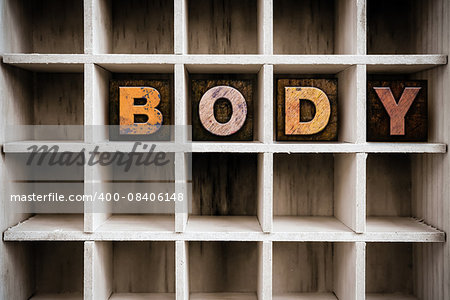 The word "BODY" written in vintage ink stained wooden letterpress type in a partitioned printer's drawer.