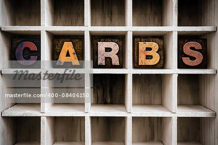 The word "CARBS" written in vintage ink stained wooden letterpress type in a partitioned printer's drawer.