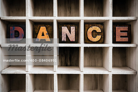 The word "DANCE" written in vintage ink stained wooden letterpress type in a partitioned printer's drawer.