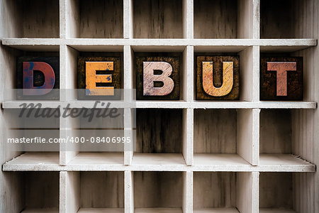 The word "DEBUT" written in vintage ink stained wooden letterpress type in a partitioned printer's drawer.