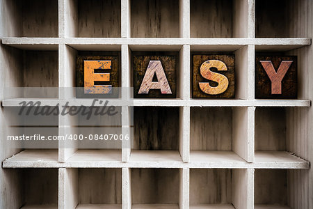 The word "EASY" written in vintage ink stained wooden letterpress type in a partitioned printer's drawer.