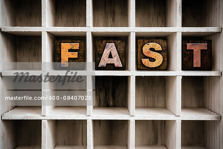 The word "FAST" written in vintage ink stained wooden letterpress type in a partitioned printer's drawer.