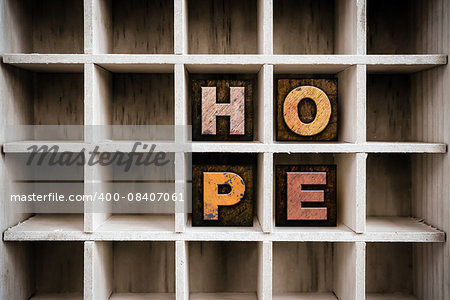 The word "HOPE" written in vintage ink stained wooden letterpress type in a partitioned printer's drawer.