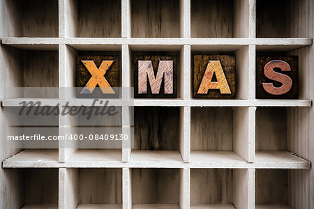 The word "XMAS" written in vintage ink stained wooden letterpress type in a partitioned printer's drawer.