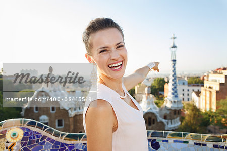 Refreshing promenade in unique Park Guell style in Barcelona, Spain. Happy young woman tourist in Park Guell, Barcelona, Spain pointing on building