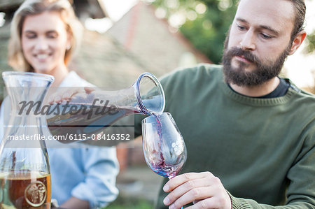 Man pouring red wine on garden party