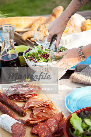 Young woman mixing salad on garden party