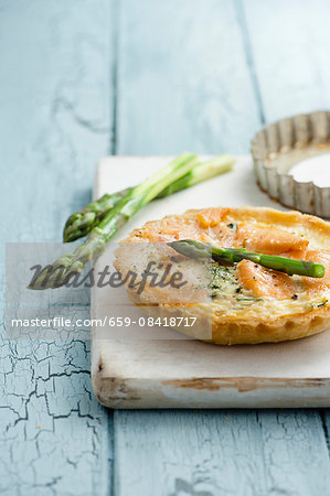 Asparagus and smoked salmon tartlets with asparagus spears on white chopping board