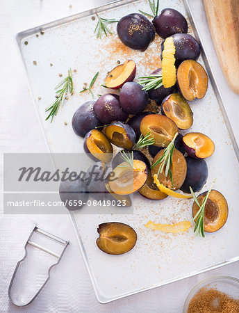 Damsons with rosemary, lemon zest and sugar on a baking tray