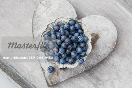 Fresh blueberries in a grey metal bowl on a heart-shaped coaster