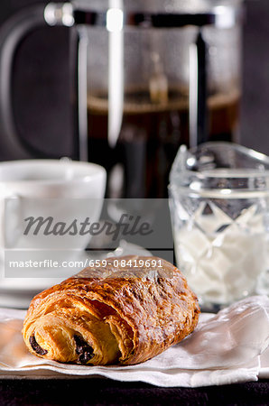 A pain au chocolat with a coffee cup and a coffee machine in the background (France)