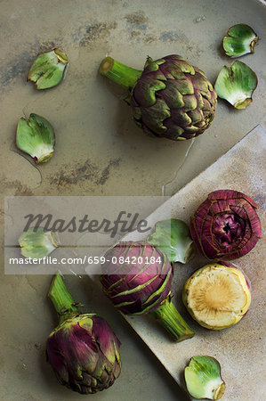 Whole artichokes, prepared artichokes and artichoke hearts on a stone platter