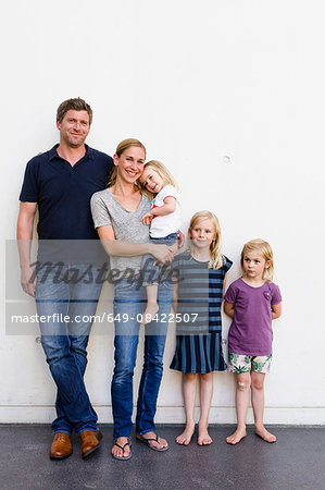 Portrait of parents and three young daughters standing in front of white wall