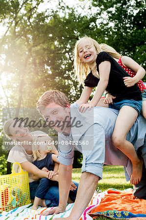 Father giving daughters piggyback at family picnic in park