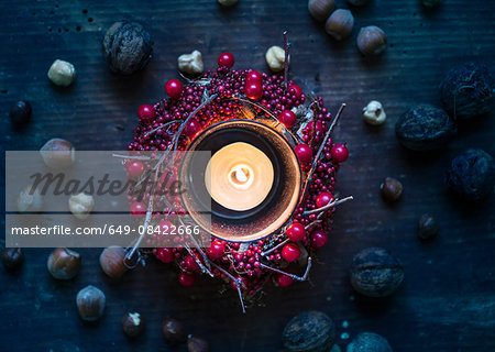 Overhead view of burning candle surrounded by berry wreath and nuts