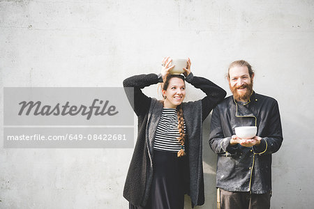 Couple standing in front of wall holding pots looking at camera smiling